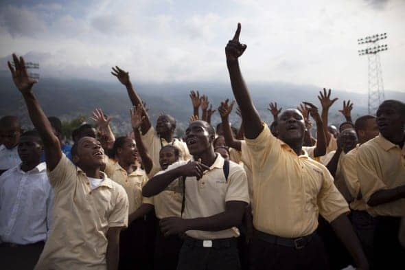 Haitians-who-lost-loved-ones-raise-hands-at-memorial-service-PAP-soccer-stadium-011211-by-Reuters, One year ago the city collapsed, World News & Views 