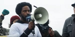 Standing-Rock-young-Black-man-on-bullhorn-at-camp-gathering-1116-vid-by-Laura-Flanders-300x150, Standing Rock: We are here to protect the water – because we all live downstream – but does eviction loom?, News & Views 