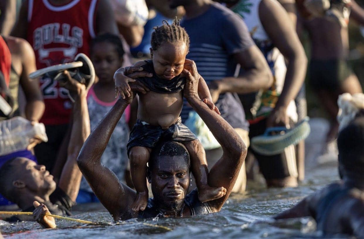 Haitian-migrant-holding-child-over-head-crossing-Rio-Grande-by-John-Moore-092021, Haitian refugee crisis made in the USA, border patrol agents whip migrants, World News & Views 