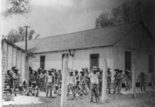 Black prisoners organize for dignity in Angola, Louisiana’s modern-day plantation Many black men in stripped prison clothes, behind barbed wire fence.