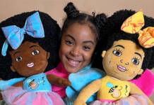 11-year-old doll creator Esi Orijin, holding one doll on the right with large blue bow in her hair with matching dress. Doll on left arm is wearing a yellow bow with a matching dress.Both dolls depict the variations of African American skin color.