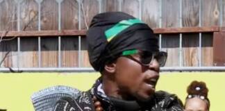 Minister King X standing with his arms crossed. Wearing African male attire, black and white weave pattern.