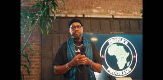 You are invited to join national Black leaders for the National Mobilization Against Genocides in Atlanta on July 4, 2026 Adult African American Male, standing with hands together at his chest, wearing a teal colored scarf, gold necklace and bracelets and black Tee-shirt. Behind him at the podium is a map of Africa representing the people.