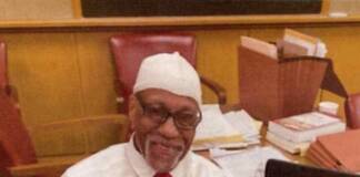 The 20-year battle to free Jeff ‘Ace’ Walker from wrongful conviction Mature man of color sitting in a brown leather chair at a desk with his laptop open. He is wearing black framed glasses, a white religious knitted cap, white shirt, red tie and black pants, hands are crossed on his left leg.